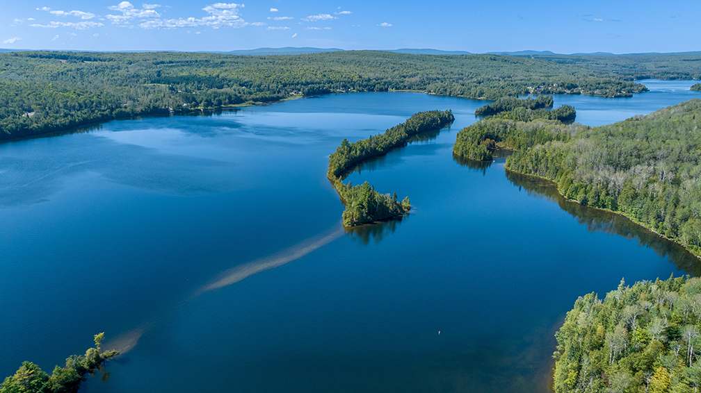 Photographie aérienne par drone d’un vaste lac entouré de forêts, mettant en valeur le territoire naturel.